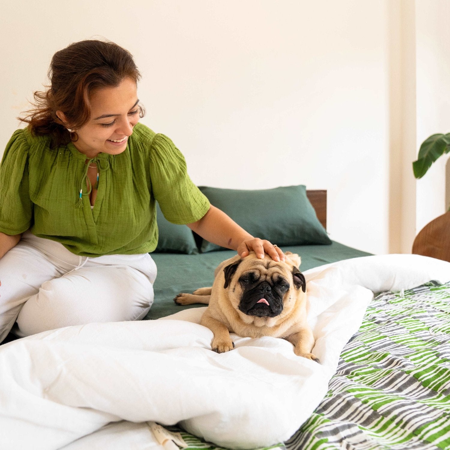 Founder petting a dog on a bed featuring the Mosswood quilt, exuding warmth and connection