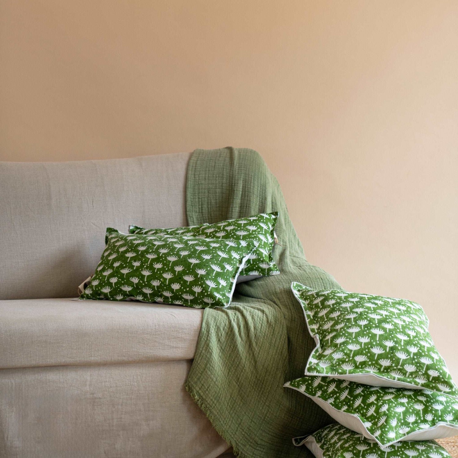 Sage green linen throw styled on a cream-colored cushion set, adding texture and warmth to a minimal living room.