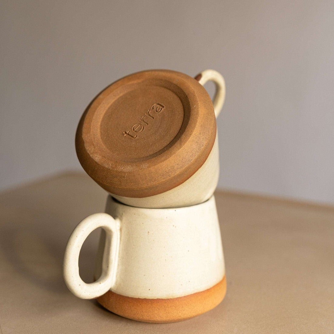 Handcrafted conical coffee mug with a smooth floating cream glaze on a wooden table.