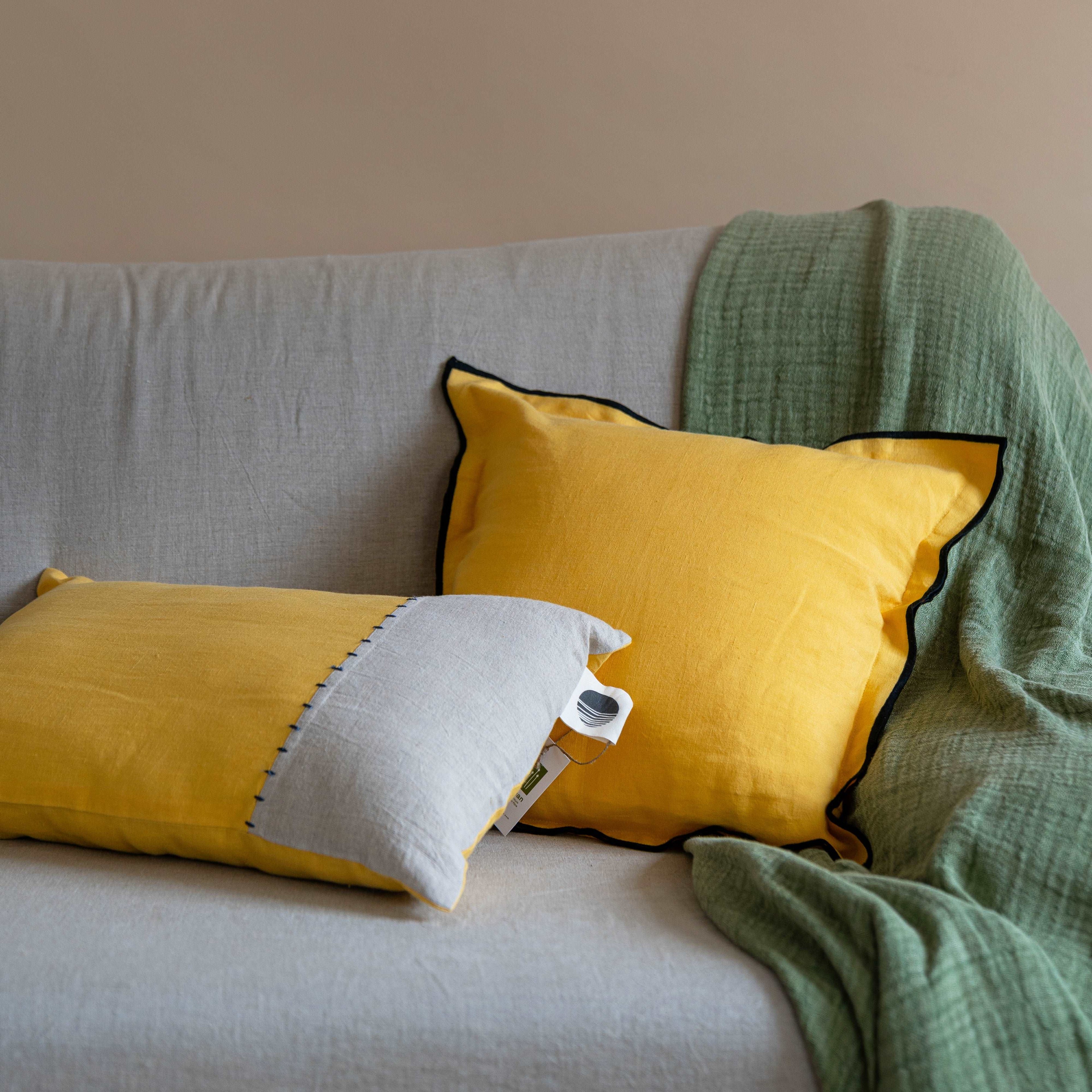 The Summer Yellow linen cushion cover placed on a modern sofa along with the half and half yellow and sand oblong, adding a pop of color to the living room décor.