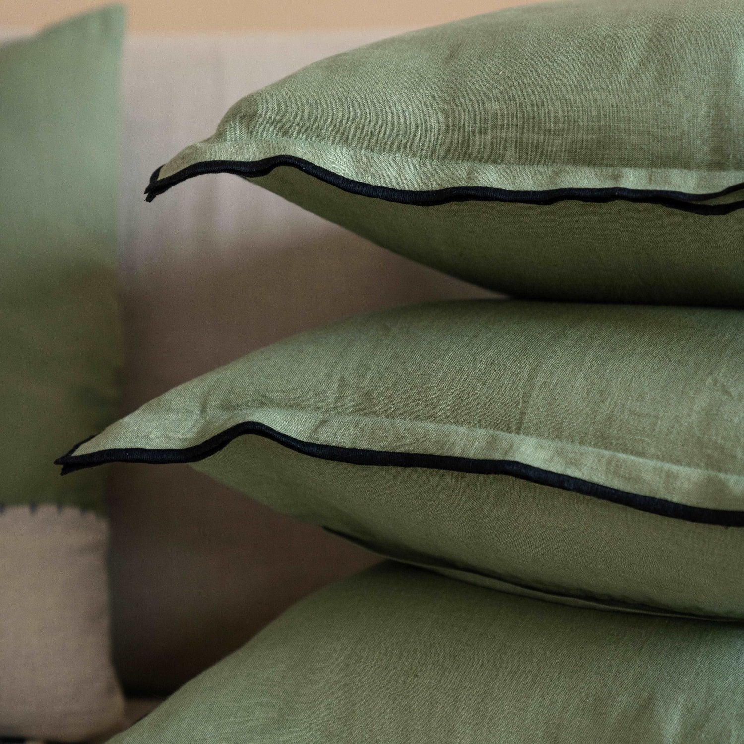 Stack of olive green linen cushion covers neatly arranged, emphasizing their craftsmanship and quality.